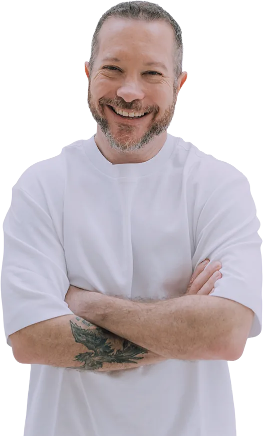 Adrián Salama sonriendo, con playera blanca y brazos cruzados